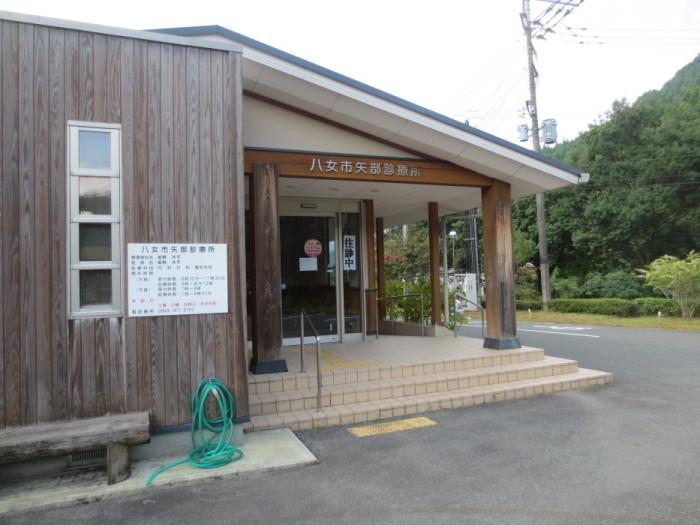 八女市矢部診療所の外観写真(左側：木造の建物で木のベンチの横の水道にホースが取り付けられている、右側：正面玄関)