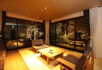 (客室)部屋に灯りが灯っており、室内には木のテーブルとソファーが置いてあり、ガラス越しに外の庭園を眺めながらゆったりとくつろげそうな部屋の写真