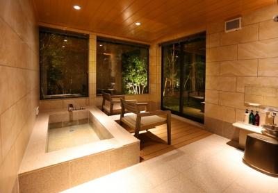 （浴室）長方形の大きな浴槽の前に椅子が2脚並べられており、ガラス越しに外の景色を眺められる夜の浴室の写真