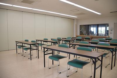 小窓を背に、長机が2つずつ並んでそれぞれ椅子が2脚ずつ設置されている実習室Bの写真