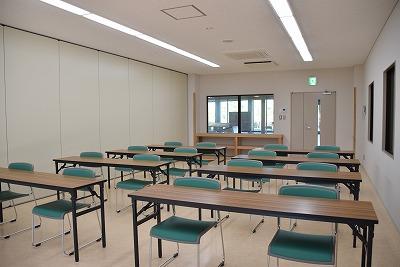 室内の入り口を背に、長机が2つずつ並んで、それぞれ椅子が2脚ずつ設置されている実習室Cの写真