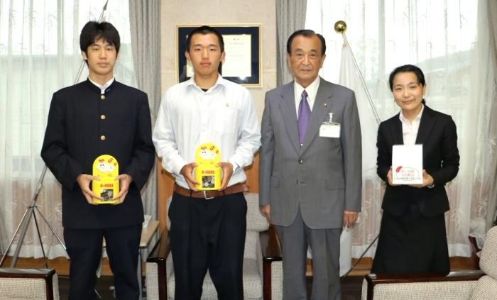 黄色の募金箱をもつ男子学生2人と委員長の弓削慶豊さん、市長の記念写真