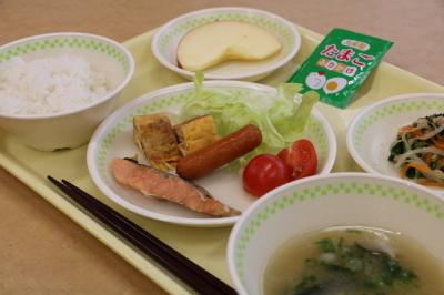 トレーの上にご飯、みそ汁、メインの焼魚、卵焼き、ウインナーやレタス、小鉢、リンゴがそれぞれ器の上に盛り付けられている朝食の写真