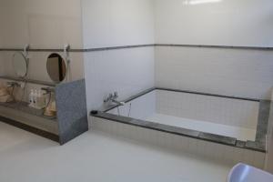 丸い鏡がそれぞれ設置されている洗い場の右横に、白色のタイルにグレー色で縁どられた正方形の形をした中浴室の室内の写真