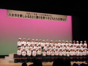 お揃いの帽子に制服姿の子供達が舞台で歌を歌っている写真