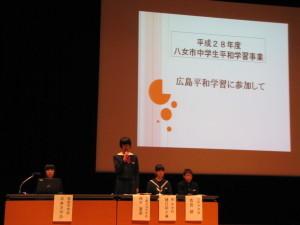 「広島平和学習に参加して」と書かれた舞台中央の大きなモニター前で4人の学生が横に並び着席しており、1人の女子学生が立ち説明をしている写真