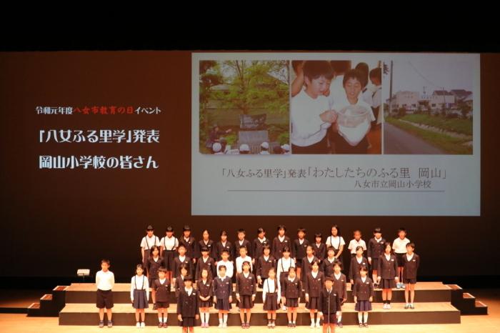 岡山小学校の生徒さんが3列に並んで舞台にたっている様子を写した写真