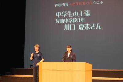 見崎中学校の川口夏未さんが舞台上で中学生の主張の発表している隣で男性が手話をしている写真