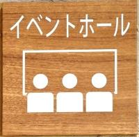 イベントホールと書かれた文字に、人の形の上を四角で囲んでいるイラストが描かれている入口の看板プレートの写真