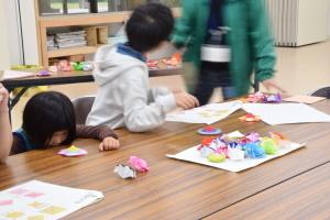 おりがみ教室に参加した男の子と女の子が、おりがみで作成し完成したコマを回して遊んでいる写真