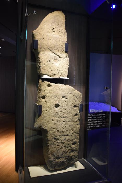ガラスケースに大きな石が立てて上下に展示されており、上は頂上が尖った形、下は複数の穴が開いている石盾の写真
