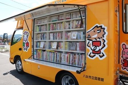 オレンジ色のトラックに猪や羊などのイラストが大きく描かれており、荷台の横から扉が上がって本棚にキレイに本が並んでいる写真
