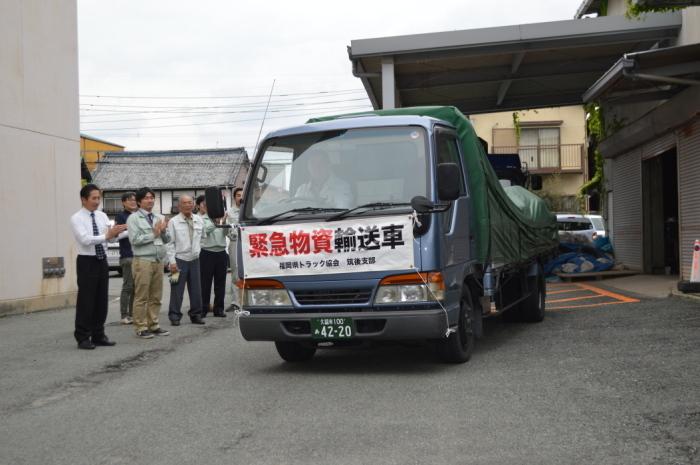 トラックの前面に緊急物資輸送車とかかれた幕が飾られている輸送車に拍手をしている人達の写真